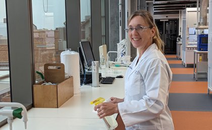 Female researcher in laboratory holding spray bottle and smiling at camera. Image, UQ